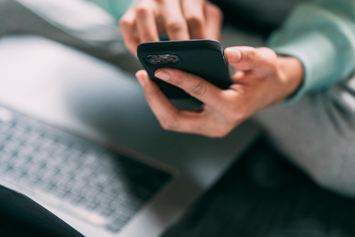 Person using a smartphone with a blurred laptop in the background